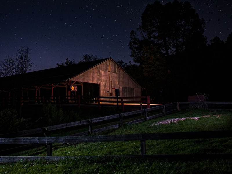 A wooden barn with its lights on at night under a starry sky